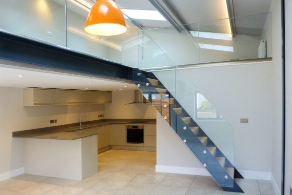 double height living space with kitchen and staircase with glass balustrade