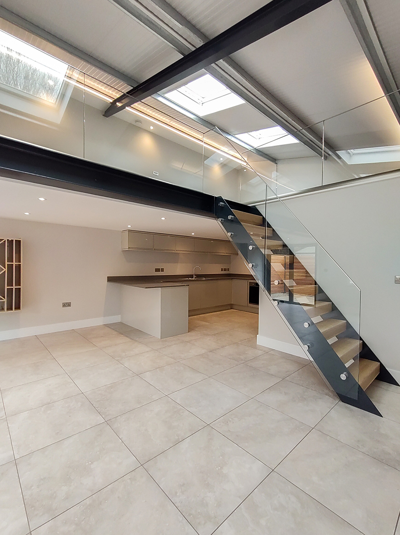 open treat staircase with glass balustrade leading to large open plan living space in barn conversion