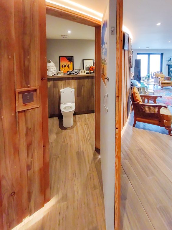 wood clad curved wall with door leading to toilet from open plan living space