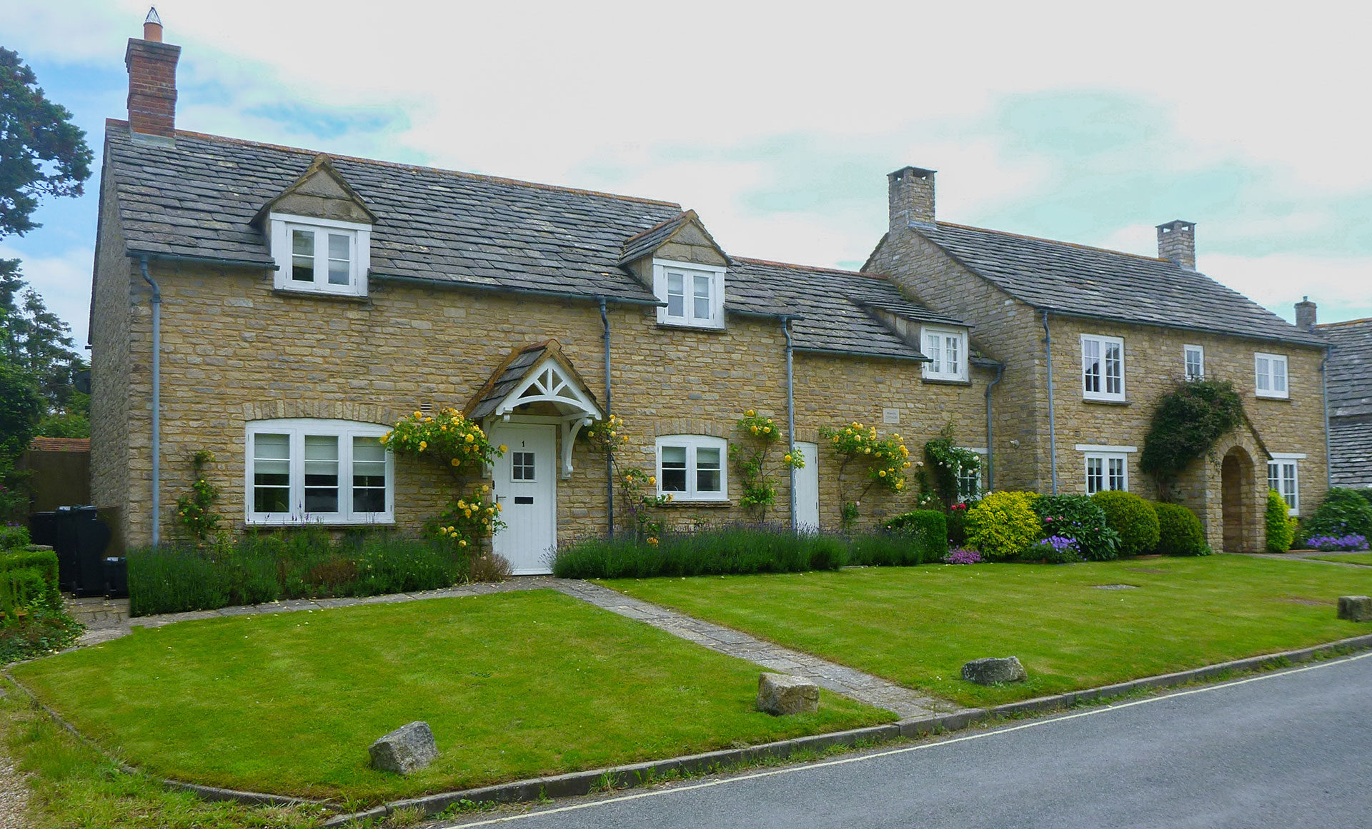 front view of traditional stone cottages with front lawns, taken from road