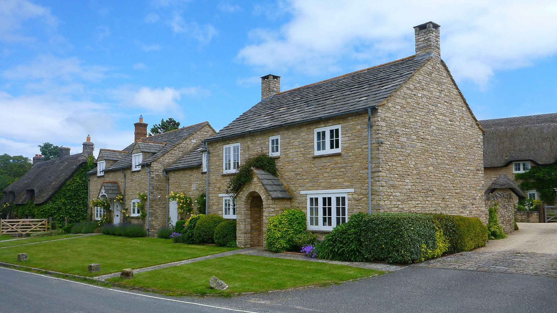 front view of traditional stone cottages with front lawns, taken from road