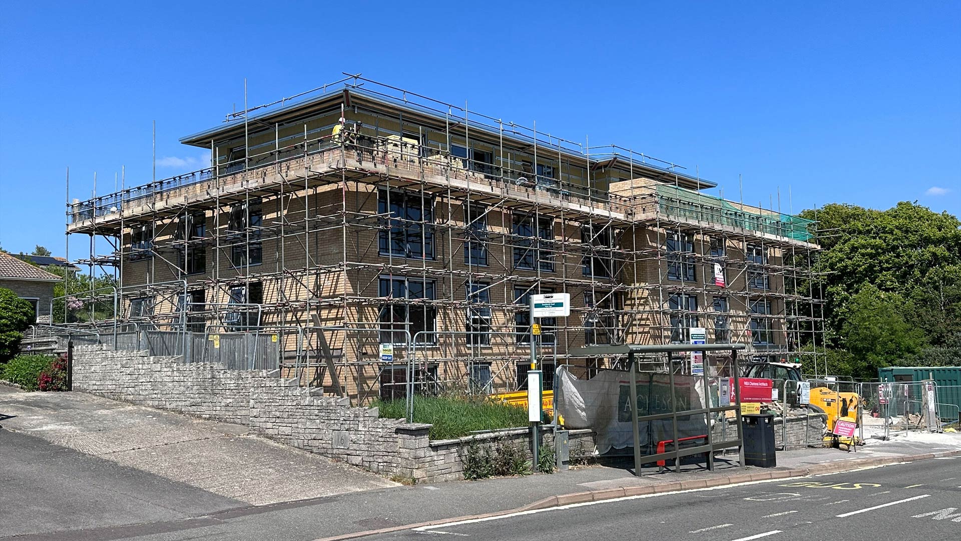 front and side view of building under construction with scaffolding from road