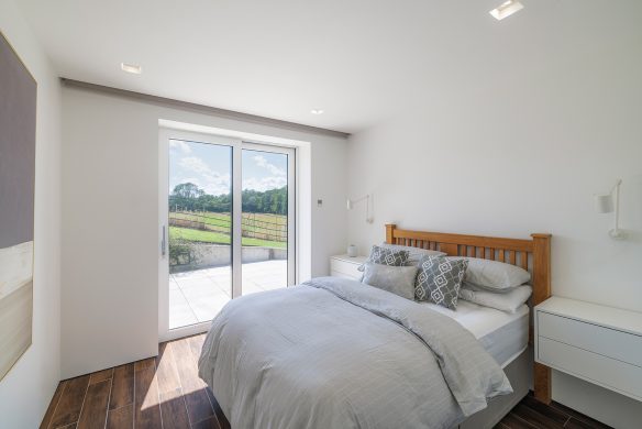 modern bedroom with white tones and wooden floor, with patio door leading to outside patio area