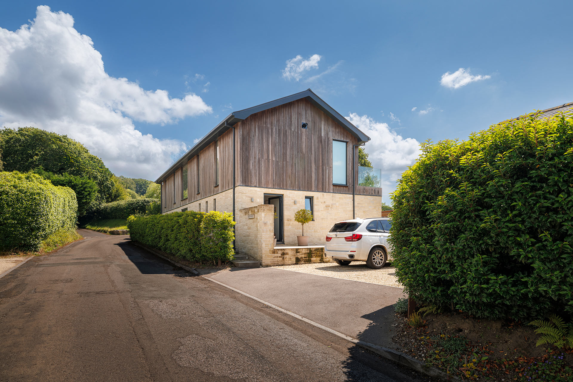 roadside approach view to house with timber clad walls and driveway