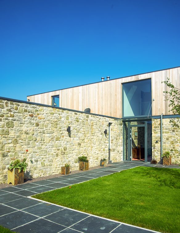 entrance approach and front garden of modern house with stone walls and timber cladding