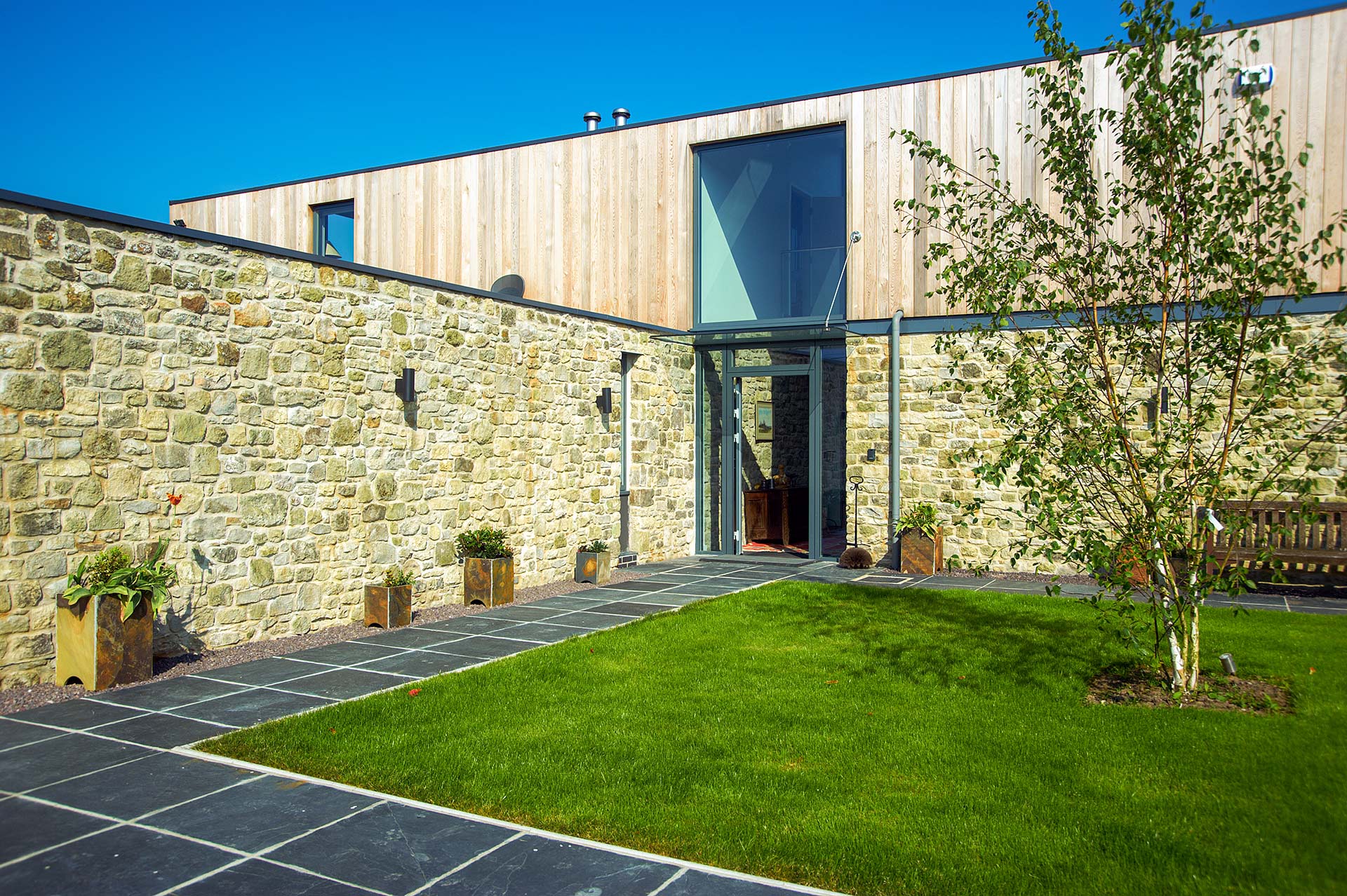 entrance approach and front garden of modern house with stone walls and timber cladding