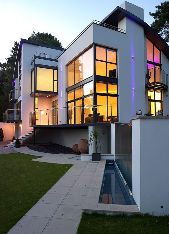 rear view of house at dusk with lights on and water feature in balcony