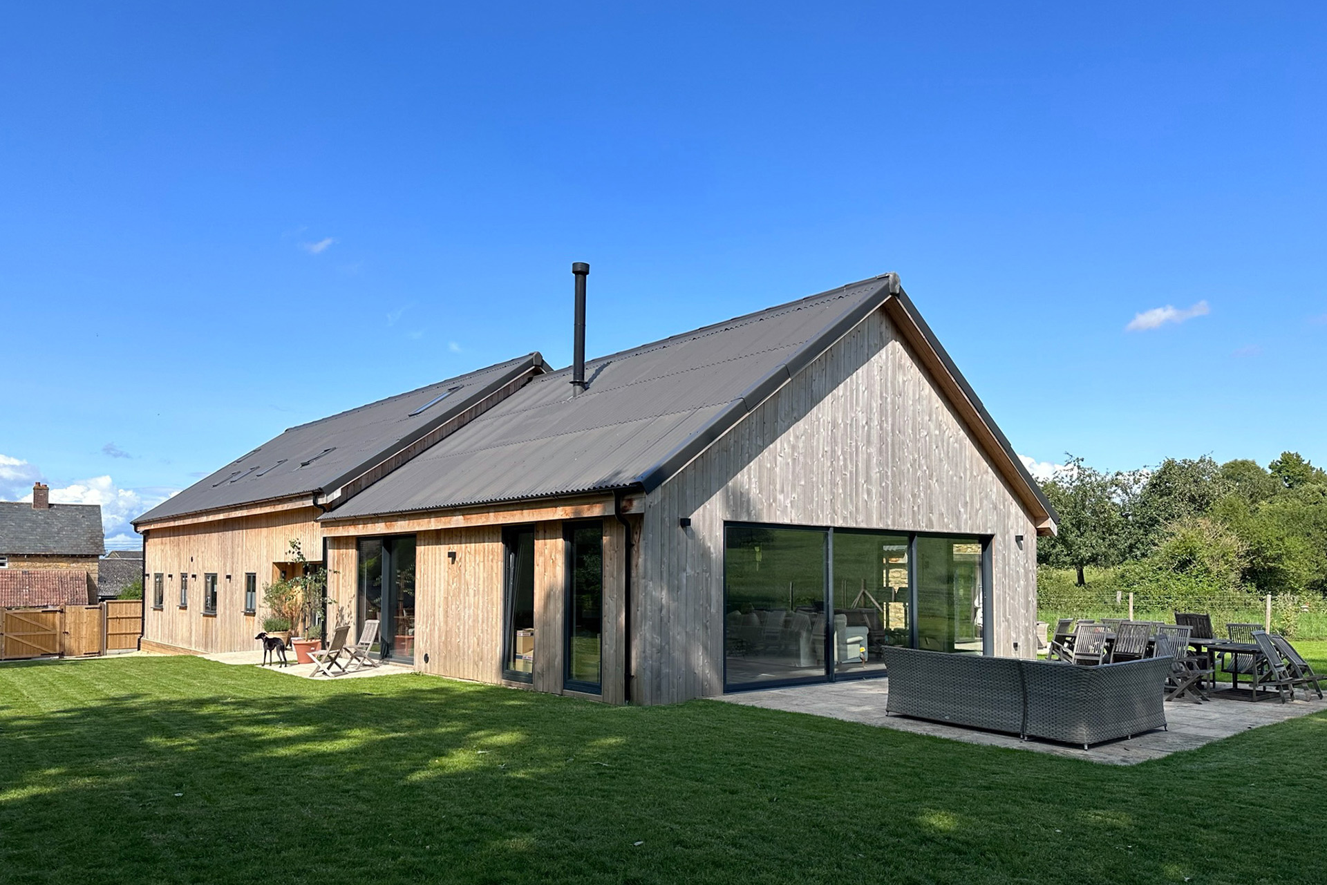rear view of barn conversion with timber clad walls and corrugated black roof with outside seating area