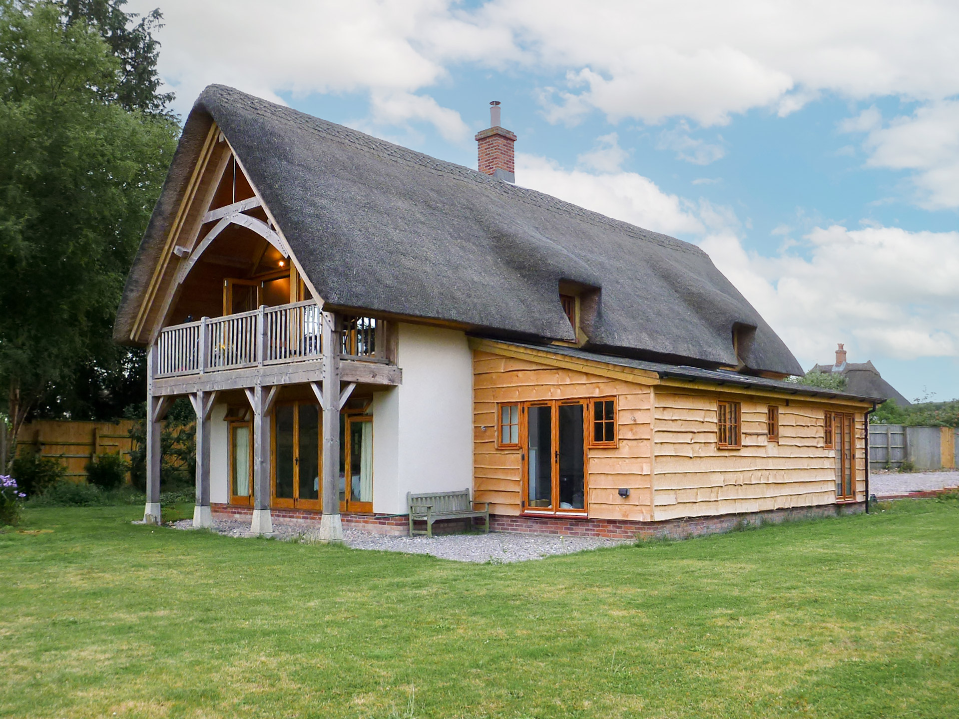 detached thatched house with wood clad extension and timber balcony