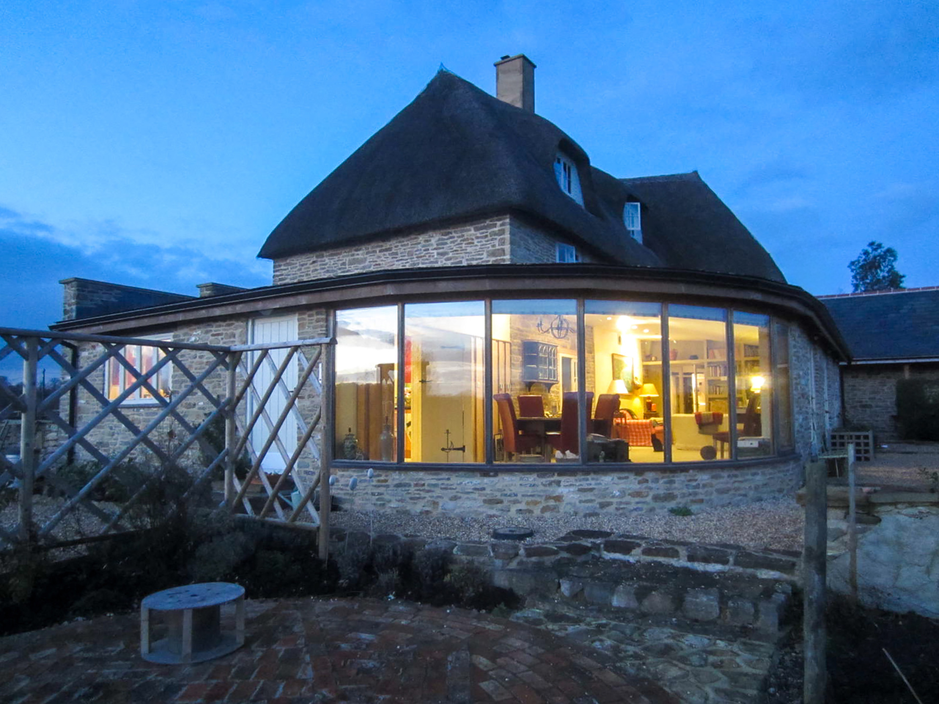 side view of extension with large windows and stone wall taken at dusk with lights on