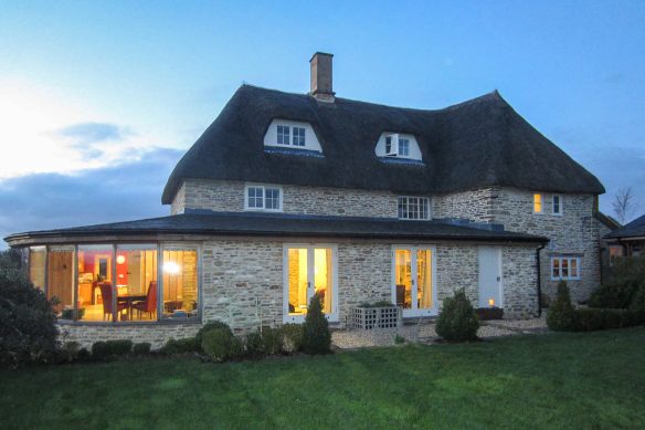 stone brick extension to thatched house at dusk with lights on