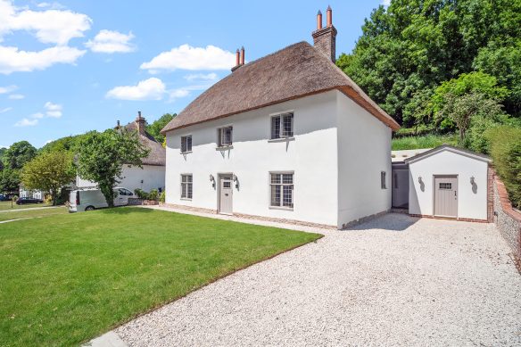 front view of white house with thatched roof and gravel driveway