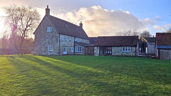 rear view of stone detached house with extension and grass lawn