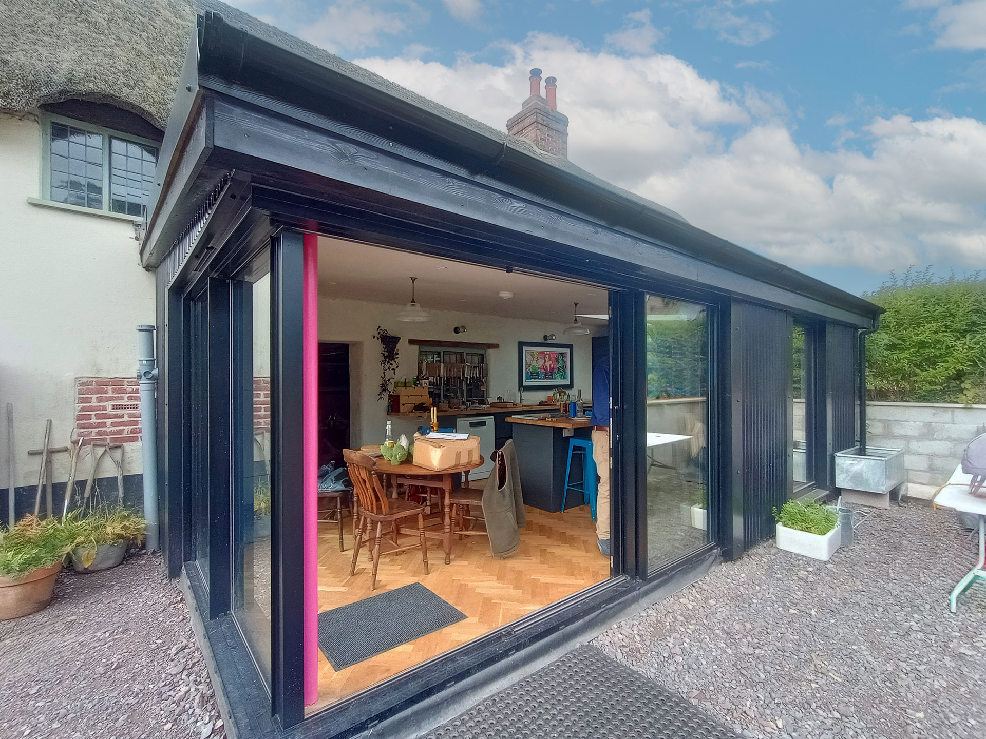 modern extension with corrugated roof attached to listed thatched cottage