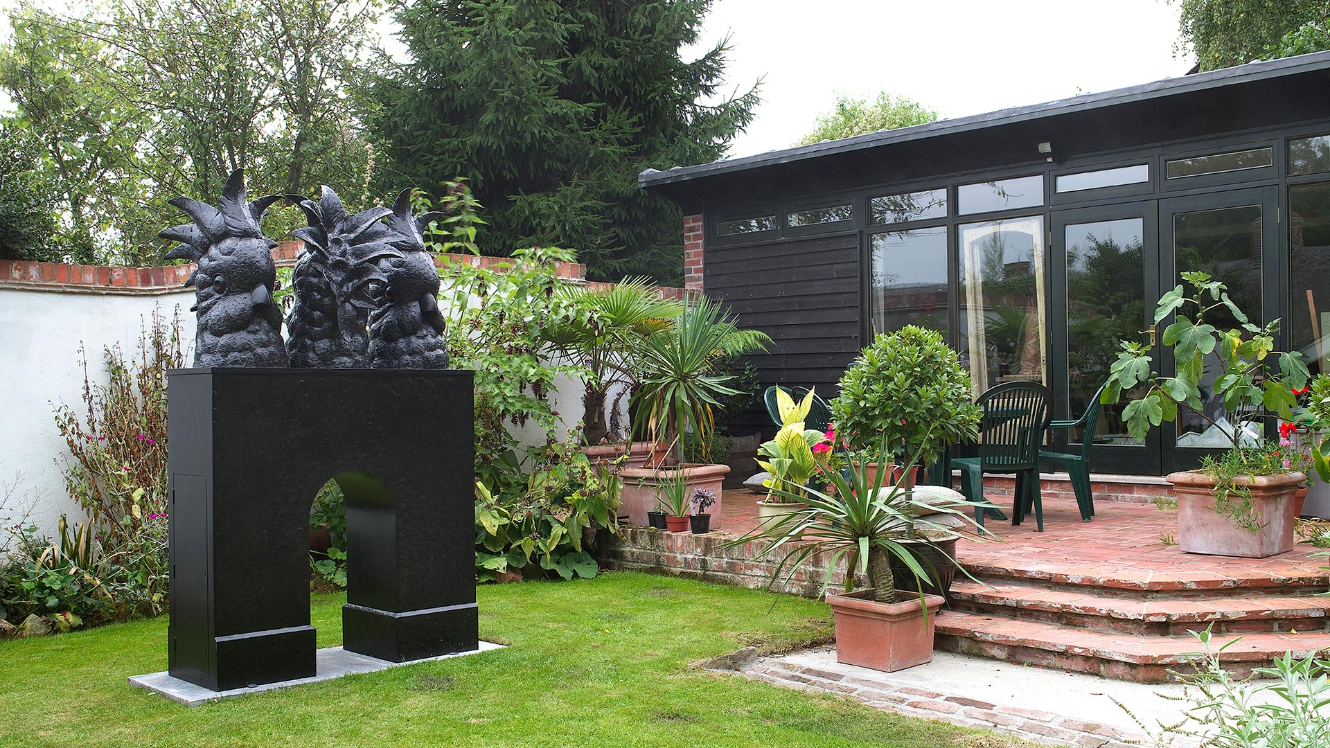 studio extension in garden with black timber cladding and statue in garden