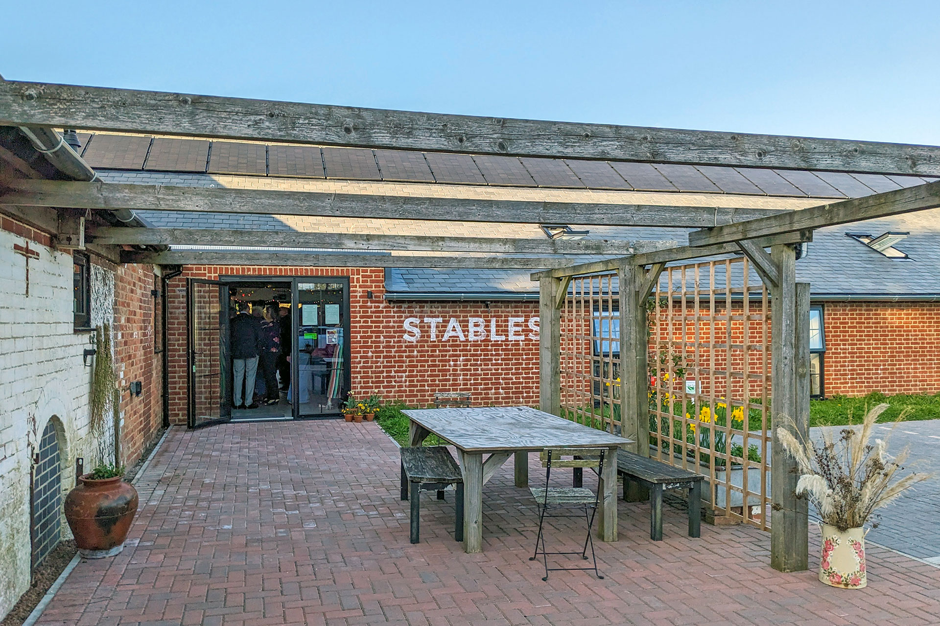 Entrance view to barn conversion with glass door and seating area under pergola