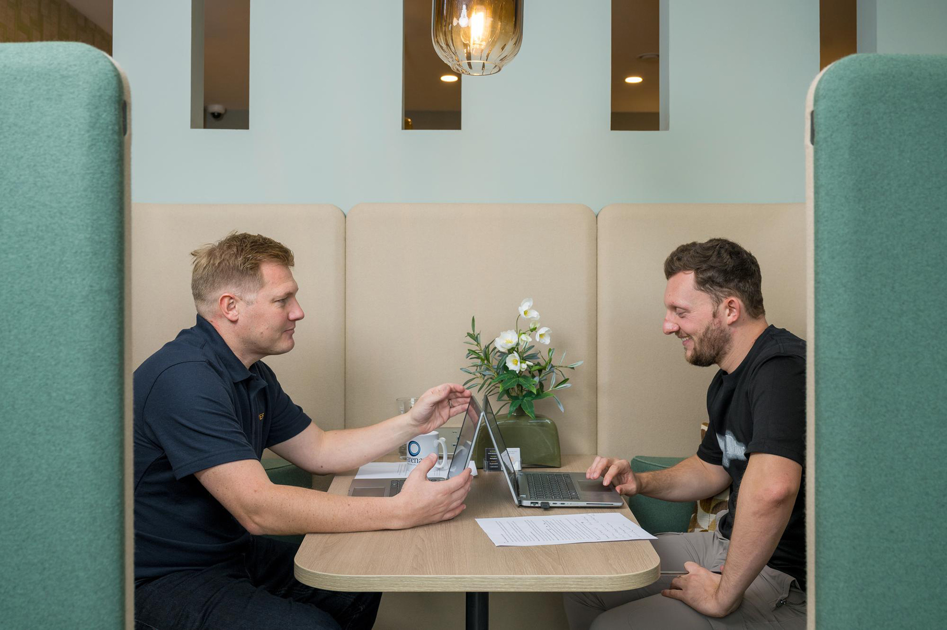 two men sitting at booth style high back chair looking at laptops
