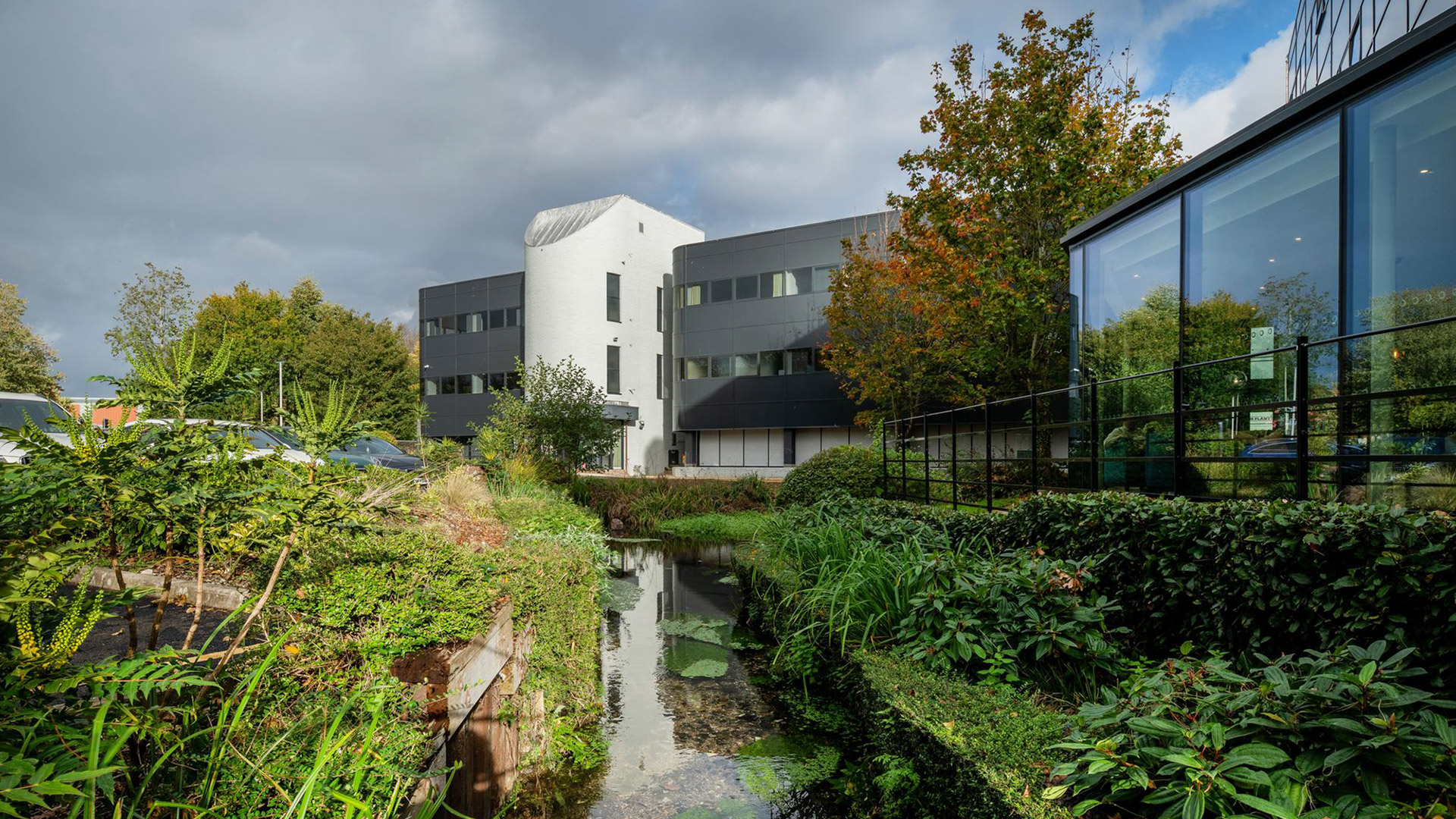 large commercial office building with black cladding and glass extension with stream in front