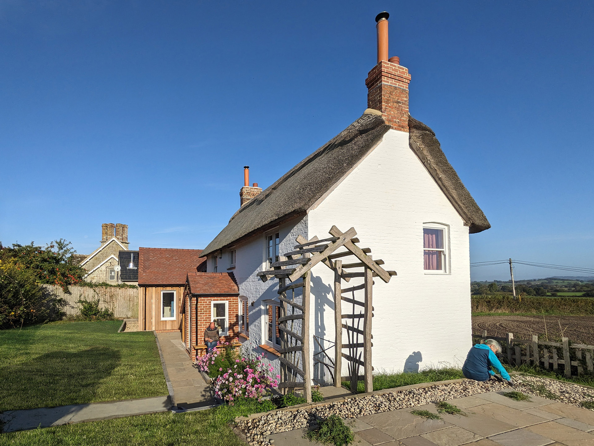Detached thatched traditional white cottage with timber clad extension