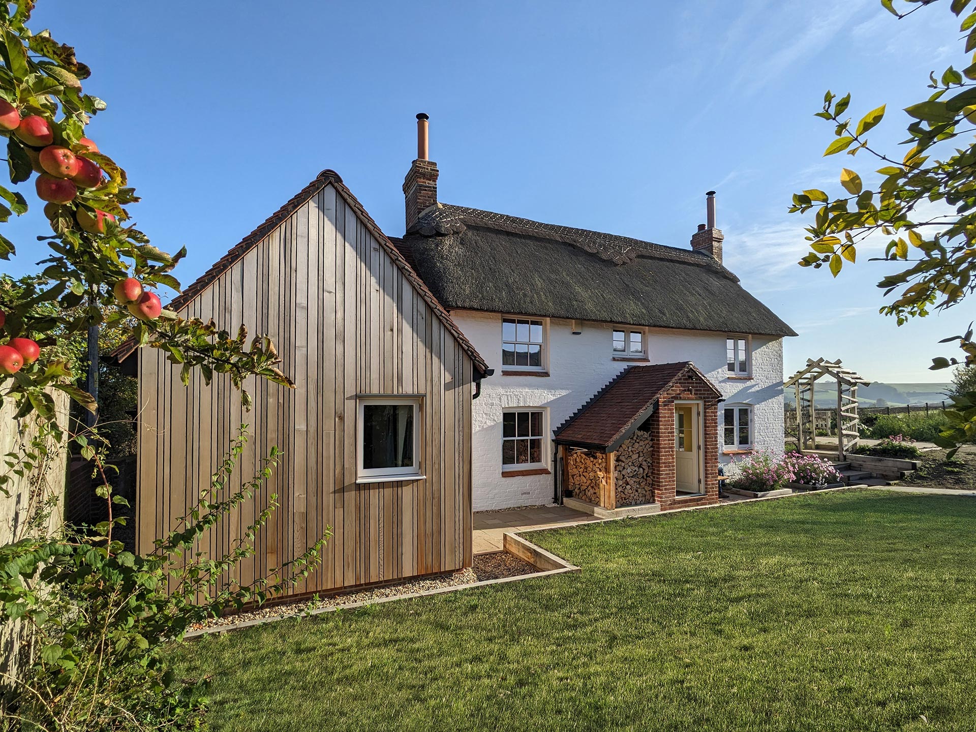 Rear side view of thatched white cottage with timber clad extension with tiled roof