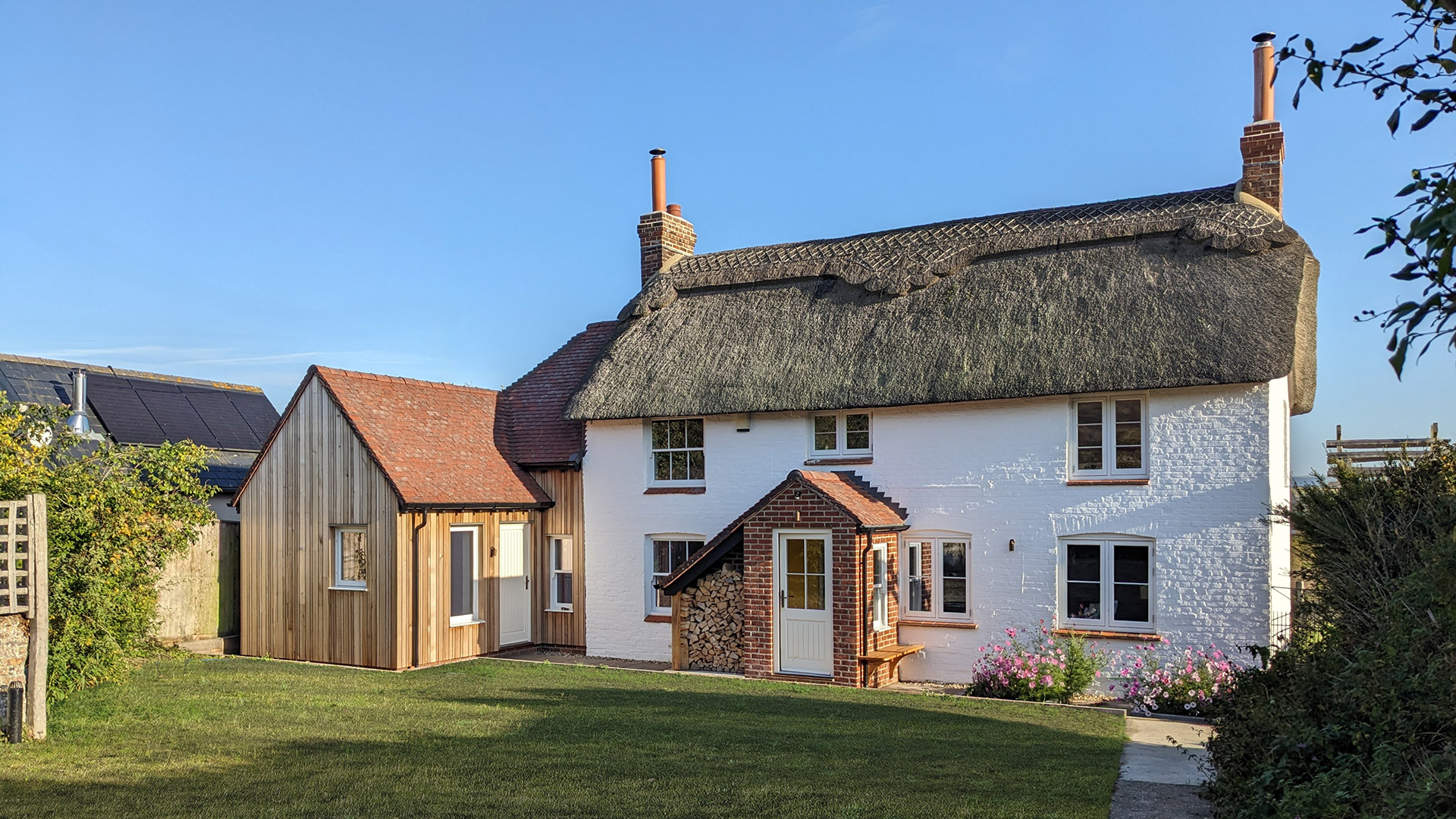 Rear view of thatched white cottage with timber clad extension with tiled roof
