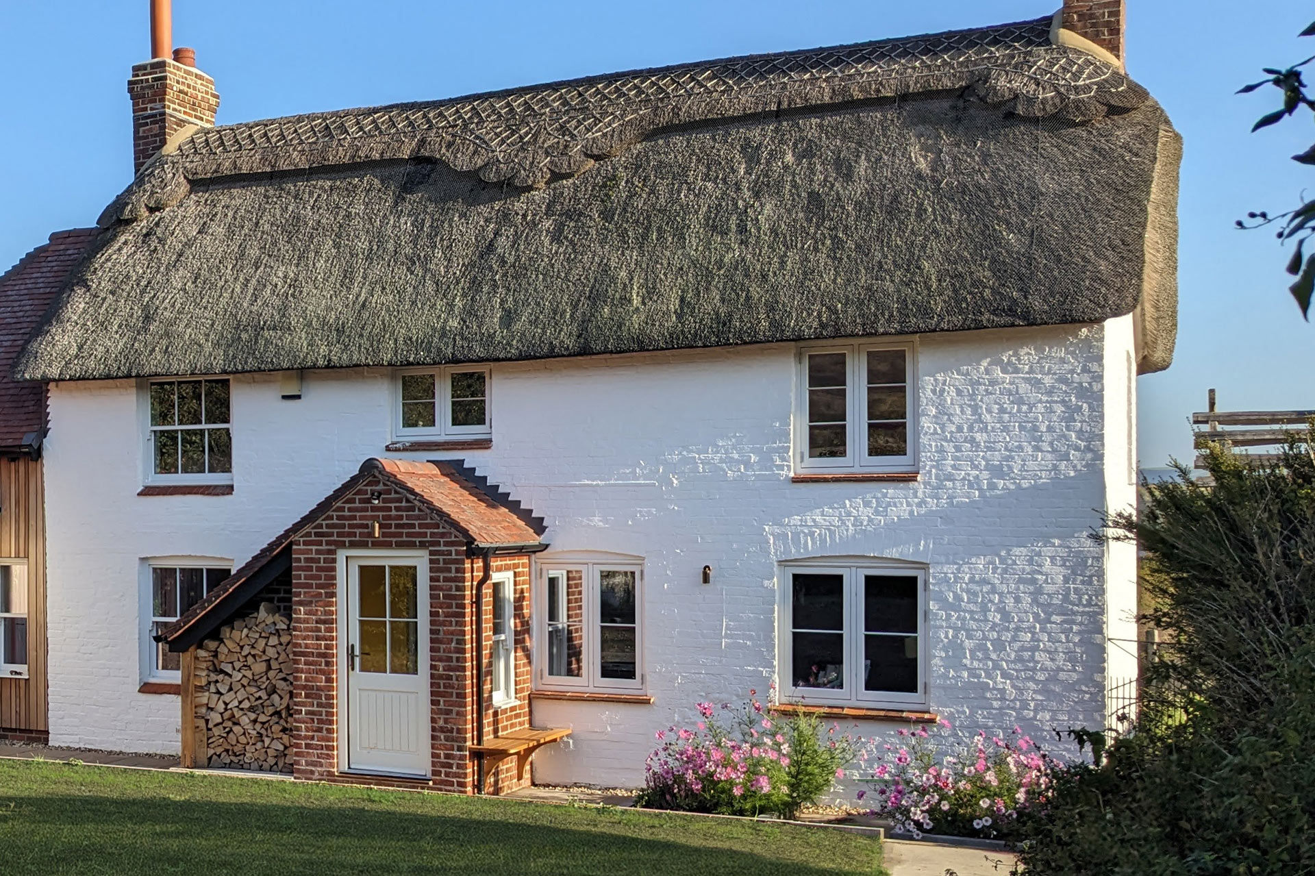 residential detached traditional white house with thatched roof with brick porch at the front and log store
