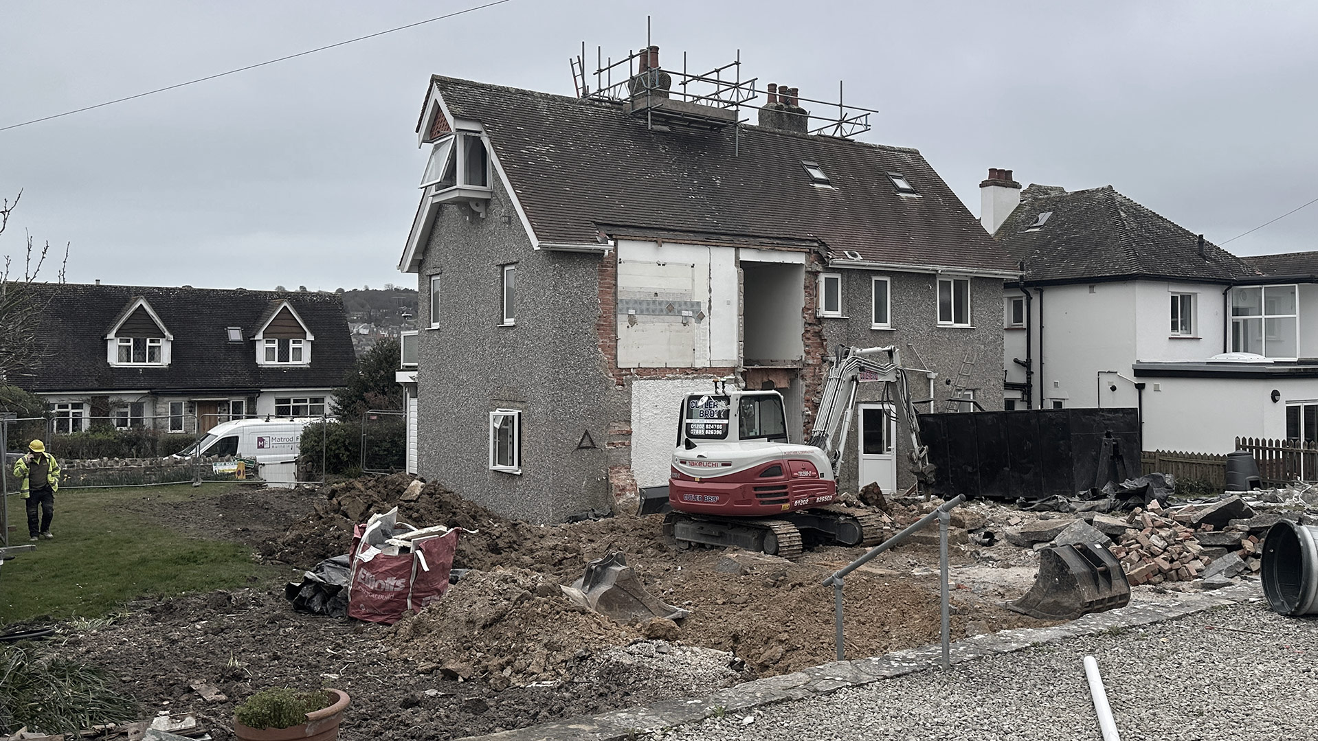 House under construction with scaffolding around chimney and excavator in the garden