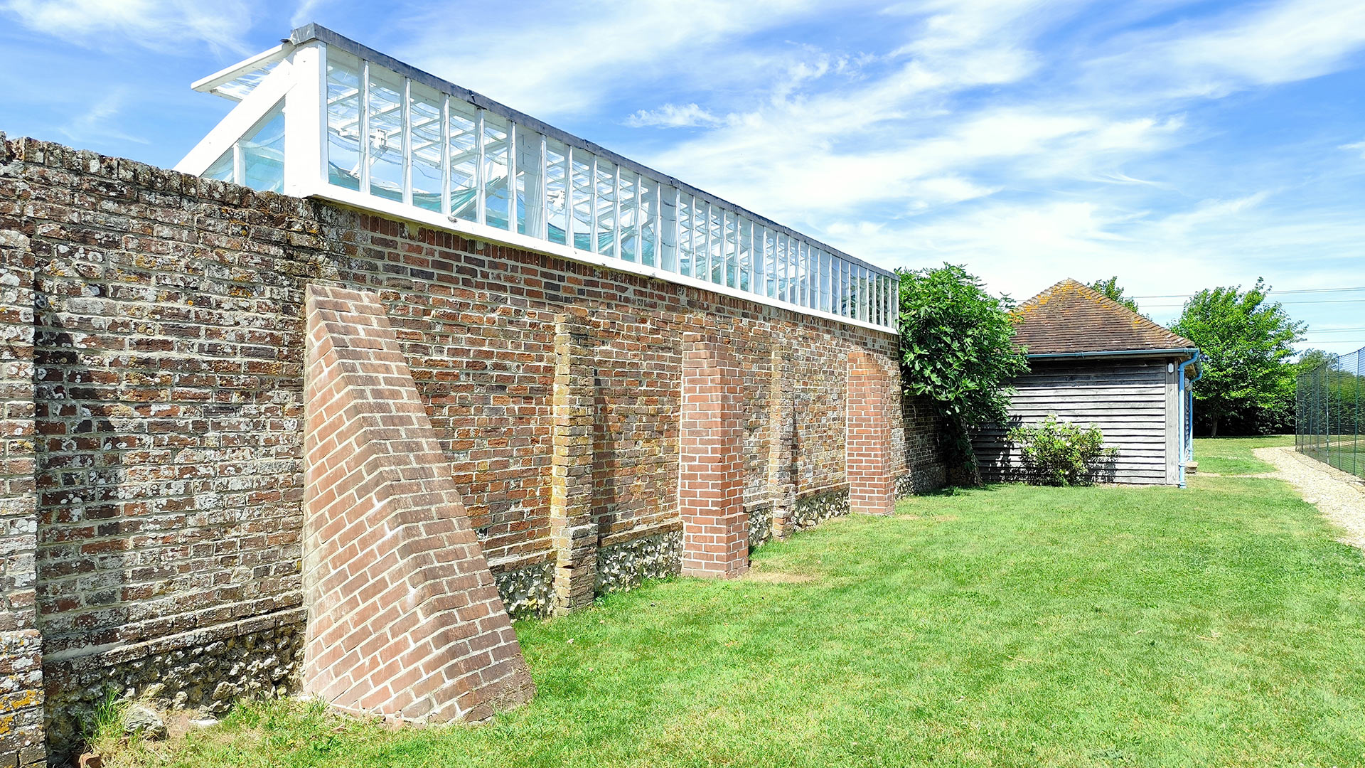 rear of a greenhouse integrated into a tall wall bordering the garden