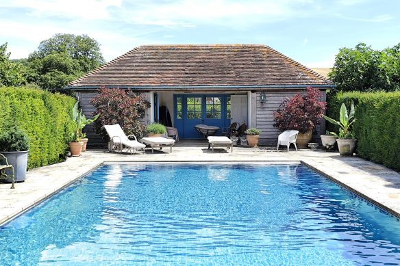 Tradition timber clad pool house with tile roof behind a blue swimming pool