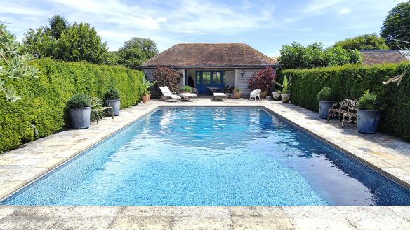 Swimming pool enclosed by hedges with a pool house at rear