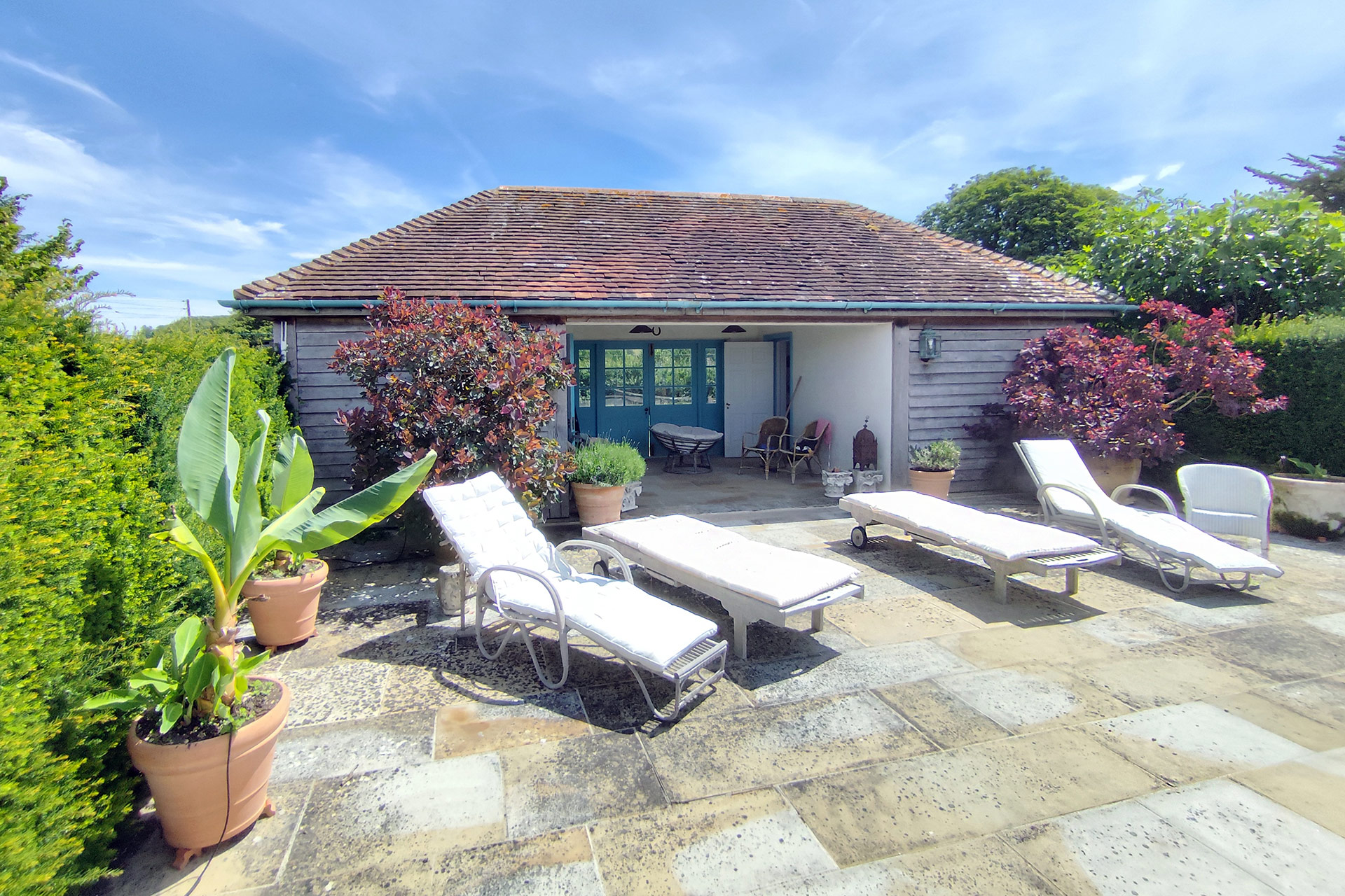 loungers in front of a timber clad traditional pool house with a tile roof