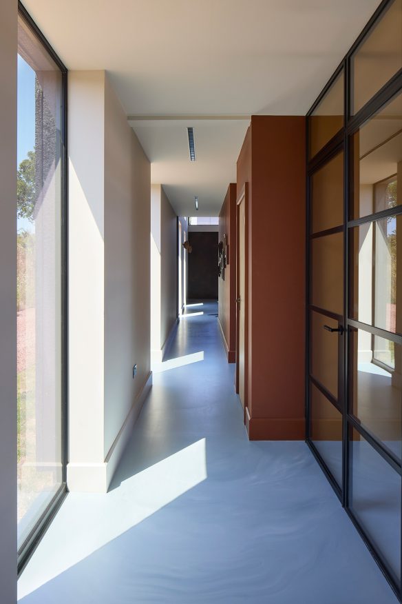 house corridor punctured with full height windows, featuring warm red painted walls